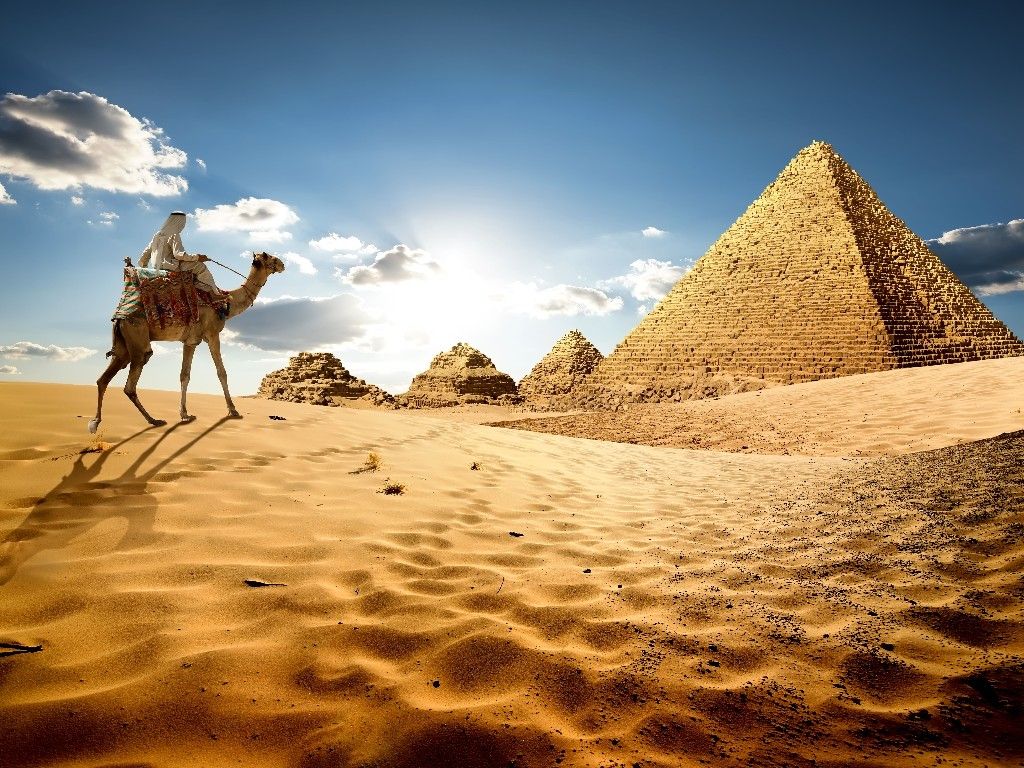 Bedouin on camel near pyramids in desert 